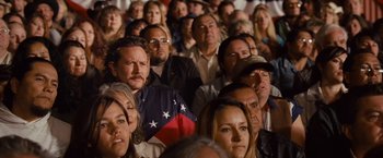 Movie still from “Swing Vote” (2008), directed by Joshua Michael Stern – A group of people sitting in a room watching a show; Medium shot, Over the shoulder angle