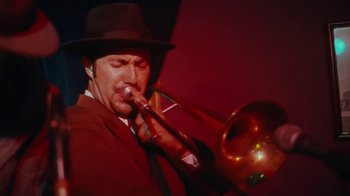 Movie still from “Swingers” (1996), directed by Doug Liman – A man in a hat playing a trombone in front of a red wall; Close Up shot, Low angle