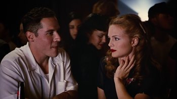 Movie still from “Swingers” (1996), directed by Doug Liman – A man and a woman sitting next to each other in front of other people; Close Up shot, Over the shoulder angle