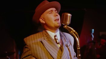 Movie still from “Swingers” (1996), directed by Doug Liman – A man wearing a suit and hat singing into a microphone; Close Up shot, Low angle