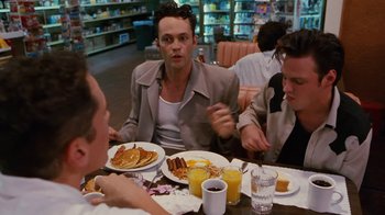 Movie still from “Swingers” (1996), directed by Doug Liman – A group of people sitting at a table with plates of food; Medium shot, Over the shoulder angle