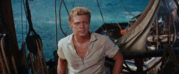 Movie still from “Swiss Family Robinson” (1960), directed by Ken Annakin – A man in a white shirt standing on top of a boat; Medium shot, High angle