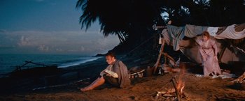 Movie still from “Swiss Family Robinson” (1960), directed by Ken Annakin – A man sitting on the ground on the beach at night; Wide shot, High angle