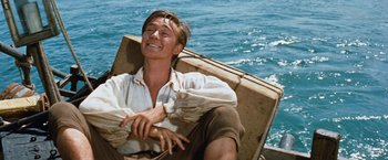 Movie still from “Swiss Family Robinson” (1960), directed by Ken Annakin – A man sitting in a boat on the water; Medium shot, High angle