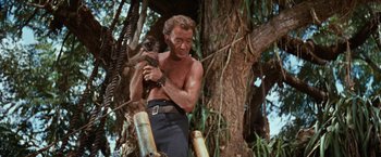Movie still from “Swiss Family Robinson” (1960), directed by Ken Annakin – A shirtless man holding a monkey in his arms; Medium shot, Low angle