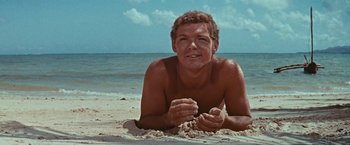 Movie still from “Swiss Family Robinson” (1960), directed by Ken Annakin – A man laying in the sand on the beach; Medium shot, Low angle