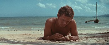 Movie still from “Swiss Family Robinson” (1960), directed by Ken Annakin – A man laying in the sand on the beach; Medium shot, Low angle