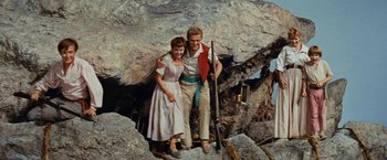 Movie still from “Swiss Family Robinson” (1960), directed by Ken Annakin – A man and a woman standing next to each other on top of rocks; Medium shot, Low angle