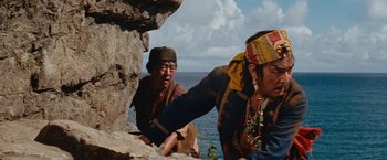 Movie still from “Swiss Family Robinson” (1960), directed by Ken Annakin – Two men are climbing a rock near the ocean; Medium shot, Over the shoulder angle