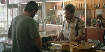 Movie still from “Sword of Trust” (2019), directed by Lynn Shelton – Two men working in a guitar shop , one of which has a guitar in his hand; Medium shot, Over the shoulder angle