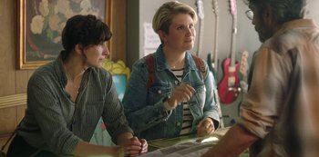 Movie still from “Sword of Trust” (2019), directed by Lynn Shelton – Two women sitting at a table in a room with guitars; Medium shot, Over the shoulder angle