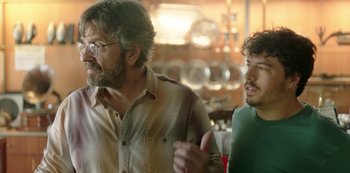 Movie still from “Sword of Trust” (2019), directed by Lynn Shelton – Two men standing next to each other in front of a table; Medium shot, Over the shoulder angle