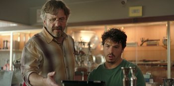 Movie still from “Sword of Trust” (2019), directed by Lynn Shelton – Two men looking at a computer screen in a room; Medium shot, Over the shoulder angle