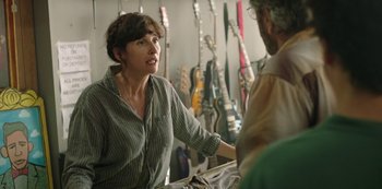 Movie still from “Sword of Trust” (2019), directed by Lynn Shelton – A woman talking to a man in a room filled with guitars; Medium shot, Over the shoulder angle