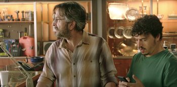 Movie still from “Sword of Trust” (2019), directed by Lynn Shelton – A man in a plaid shirt is standing in front of a counter; Medium shot, Over the shoulder angle