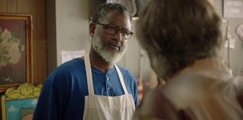 An older man wearing an apron talking to a woman