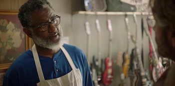 Movie still from “Sword of Trust” (2019), directed by Lynn Shelton – An older man wearing an apron in front of a row of electric guitars; Close Up shot, Over the shoulder angle