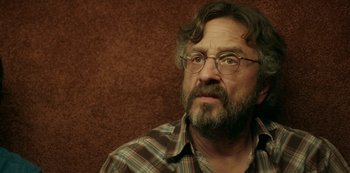 Movie still from “Sword of Trust” (2019), directed by Lynn Shelton – A man with a beard wearing glasses and a plaid shirt; Close Up shot, Over the shoulder angle