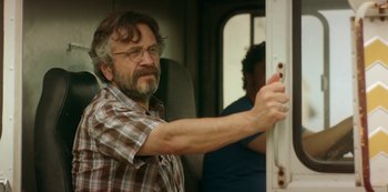 Movie still from “Sword of Trust” (2019), directed by Lynn Shelton – A man with a beard and glasses on a train; Close Up shot, Over the shoulder angle