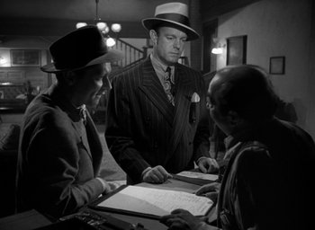 Movie still from “T-Men” (1947), directed by Anthony Mann – A man in a suit and hat standing next to two other men; Medium shot, Over the shoulder angle