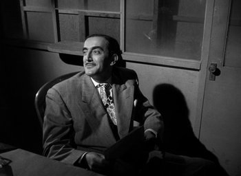 Movie still from “T-Men” (1947), directed by Anthony Mann – A man sitting at a desk in a suit and tie; Medium shot, Low angle