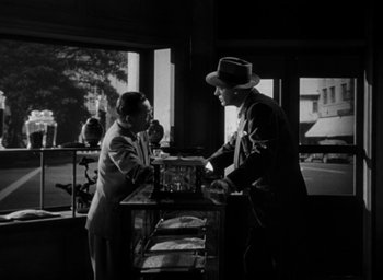 Movie still from “T-Men” (1947), directed by Anthony Mann – Two men standing at a table in front of a window; Medium shot, Low angle