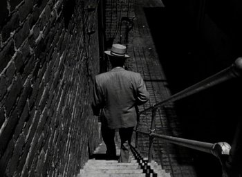 Movie still from “T-Men” (1947), directed by Anthony Mann – A black and white photo of a man walking up a flight of stairs; Wide shot, High angle