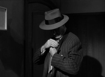 Movie still from “T-Men” (1947), directed by Anthony Mann – A black and white photo of a man wearing a hat and a suit; Medium shot, Low angle
