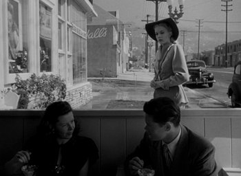 Movie still from “T-Men” (1947), directed by Anthony Mann – A man and a woman sitting in front of a store window; Wide shot, Over the shoulder angle