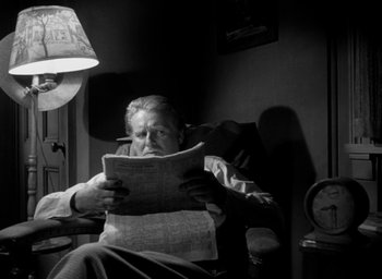 Movie still from “T-Men” (1947), directed by Anthony Mann – An older man sitting in a chair reading a newspaper; Medium shot, Low angle