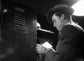 Movie still from “T-Men” (1947), directed by Anthony Mann – A black and white photo of a man in a suit and hat looking down at a piece of paper; Close Up shot, Low angle