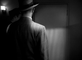 Movie still from “T-Men” (1947), directed by Anthony Mann – A black and white photo of a man in a suit and a hat; Medium shot, Over the shoulder angle