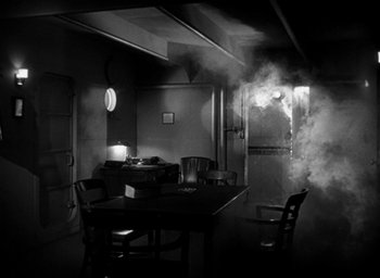 Movie still from “T-Men” (1947), directed by Anthony Mann – A table and chairs in a dark room with smoke coming out of the door; Wide shot, High angle