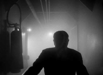 Movie still from “T-Men” (1947), directed by Anthony Mann – A man standing in a dark room with lights; Wide shot, Low angle
