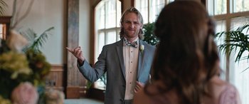 Movie still from “Table 19” (2017), directed by Jeffrey Blitz – A man in a suit and bow tie standing in front of a window; Medium shot, Over the shoulder angle