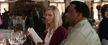 Movie still from “Table 19” (2017), directed by Jeffrey Blitz – A woman is reading a book while a man looks on; Close Up shot, Over the shoulder angle