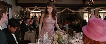 Movie still from “Table 19” (2017), directed by Jeffrey Blitz – A woman in a pink dress standing at a dinner table; Medium shot, Over the shoulder angle