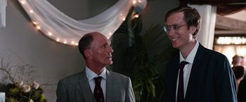 Movie still from “Table 19” (2017), directed by Jeffrey Blitz – A man in a suit and tie standing next to another man in a suit and tie; Close Up shot, Over the shoulder angle