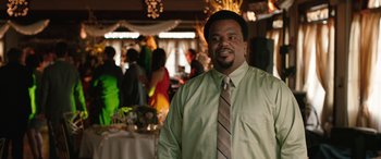 Movie still from “Table 19” (2017), directed by Jeffrey Blitz – A man standing in front of a crowd of people at an event; Medium shot, Over the shoulder angle