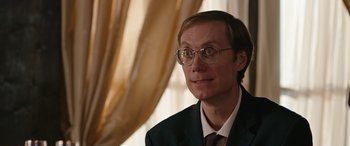 Movie still from “Table 19” (2017), directed by Jeffrey Blitz – A person wearing a suit and glasses; Close Up shot, Over the shoulder angle