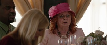Movie still from “Table 19” (2017), directed by Jeffrey Blitz – An older woman wearing a pink hat with a flower on it; Close Up shot, Over the shoulder angle