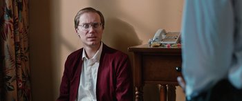 Movie still from “Table 19” (2017), directed by Jeffrey Blitz – A man sitting in front of a wooden desk; Close Up shot, High angle
