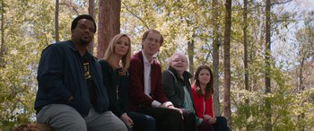 Movie still from “Table 19” (2017), directed by Jeffrey Blitz – A group of people sitting next to each other on top of a bench; Medium shot, Over the shoulder angle