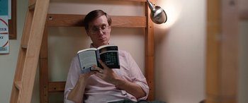 Movie still from “Table 19” (2017), directed by Jeffrey Blitz – A man sitting in a chair while reading a book; Medium shot, High angle
