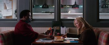 Movie still from “Table 19” (2017), directed by Jeffrey Blitz – Two people sitting at a table in front of a laptop; Medium shot, Over the shoulder angle
