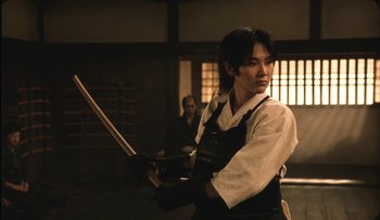 Movie still from “Taboo” (1999), directed by Nagisa Ôshima – A person holding a sword in a room; Medium shot, Over the shoulder angle