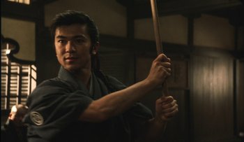 Movie still from “Taboo” (1999), directed by Nagisa Ôshima – A man holding a wooden stick in his hands; Close Up shot, Low angle