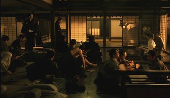 Movie still from “Taboo” (1999), directed by Nagisa Ôshima – A group of people sitting in a dark room; Wide shot, High angle