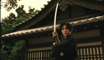 Movie still from “Taboo” (1999), directed by Nagisa Ôshima – A man holding a sword in front of a building; Medium shot, Low angle