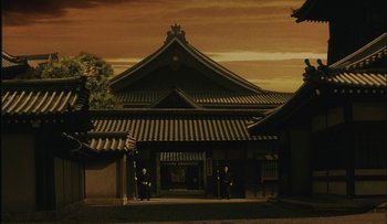 Movie still from “Taboo” (1999), directed by Nagisa Ôshima – An asian style building with two men standing in front of it at sunset; Extreme Wide shot, Low angle